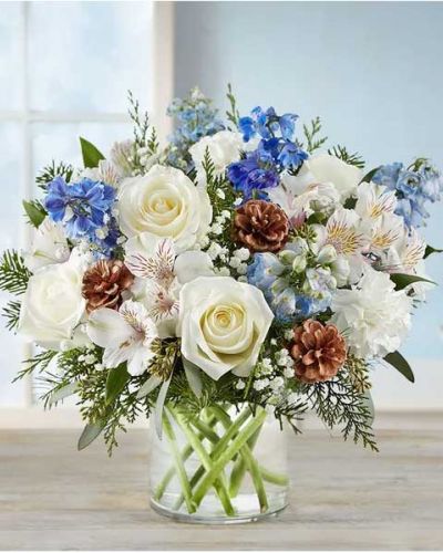 Inspired by winter’s cool blue & white landscape, our delightful arrangement delivers warm wishes to the people you love. Hand-designed with a lush gathering of blooms, evergreens and rustic touches, it’s a thoughtful sentiment filled with the season’s natural beauty.
<ul>
 	<li>All-around arrangement with white roses, carnations and Peruvian lilies (alstroemeria); blue delphinium; accented with baby’s breath, seeded eucalyptus, assorted Christmas greenery and pinecones</li>
 	<li>Artistically designed in a clear glass cylinder vase</li>
 	<li>Large arrangement measures approximately 15"H x 13"W</li>
 	<li>Medium arrangement measures approximately 13"H x 12"W</li>
 	<li>Small arrangement measures approximately 12"H x 9"W</li>
 	<li>Our florists hand-design each arrangement, so colors, varieties and container may vary due to local availability</li>
 	<li>To ensure lasting beauty, Peruvian lilies may arrive in bud form and will fully bloom over the next few days</li>
</ul>